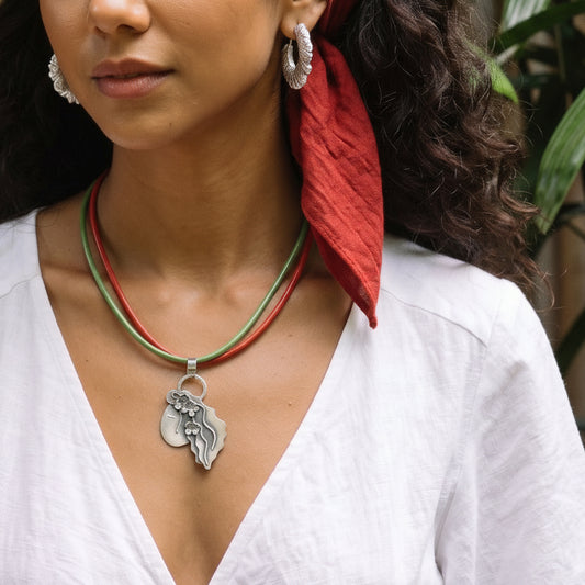 Lullaby necklace worn on a green and red cord over a white shirt