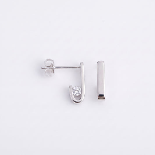 Pair of J-02 silver earrings on a white background: one seen from the side with the clear zircon in its curve and its post, the other from the front as a straight line