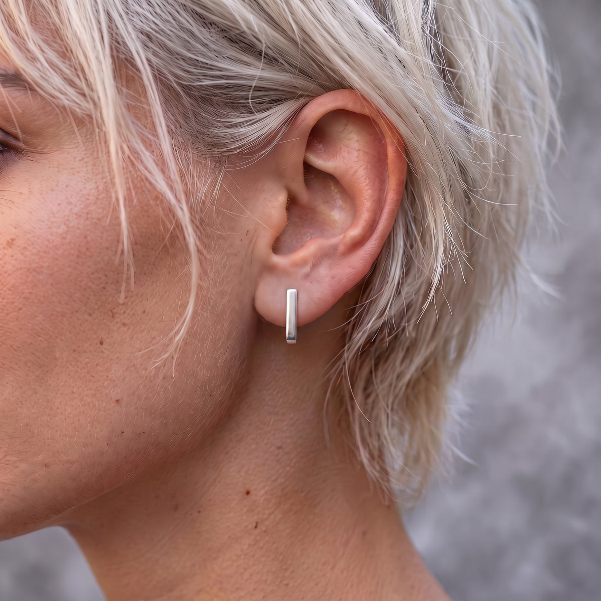 J-02 earring on the ear of a woman with short blonde hair, seen from the front as a straight silver line
