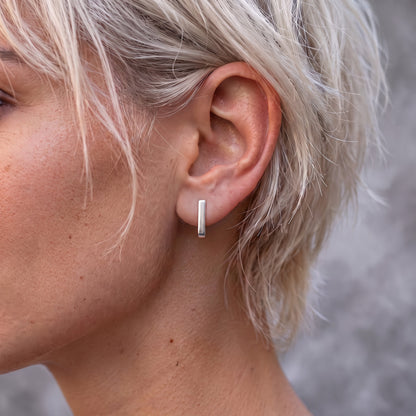 J-02 earring on the ear of a woman with short blonde hair, seen from the front as a straight silver line