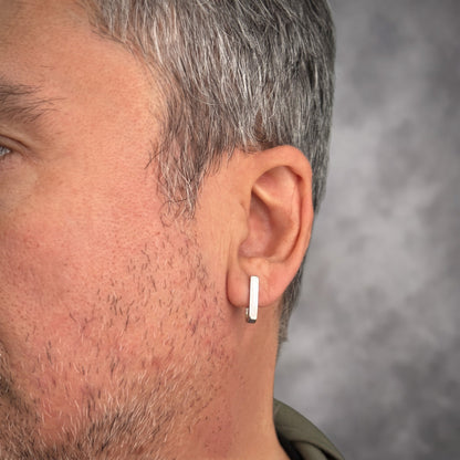 J-02 silver bar earring on the ear of a grey-haired, bearded man, close-up