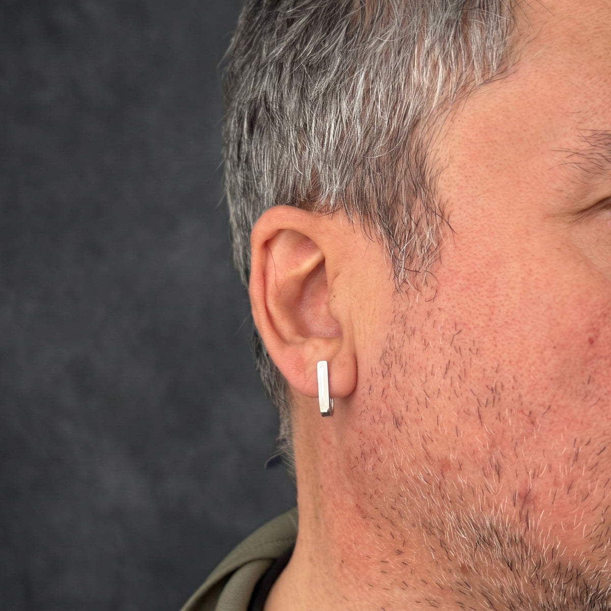 J-02 silver bar earring on a male model's ear, in profile against a dark background