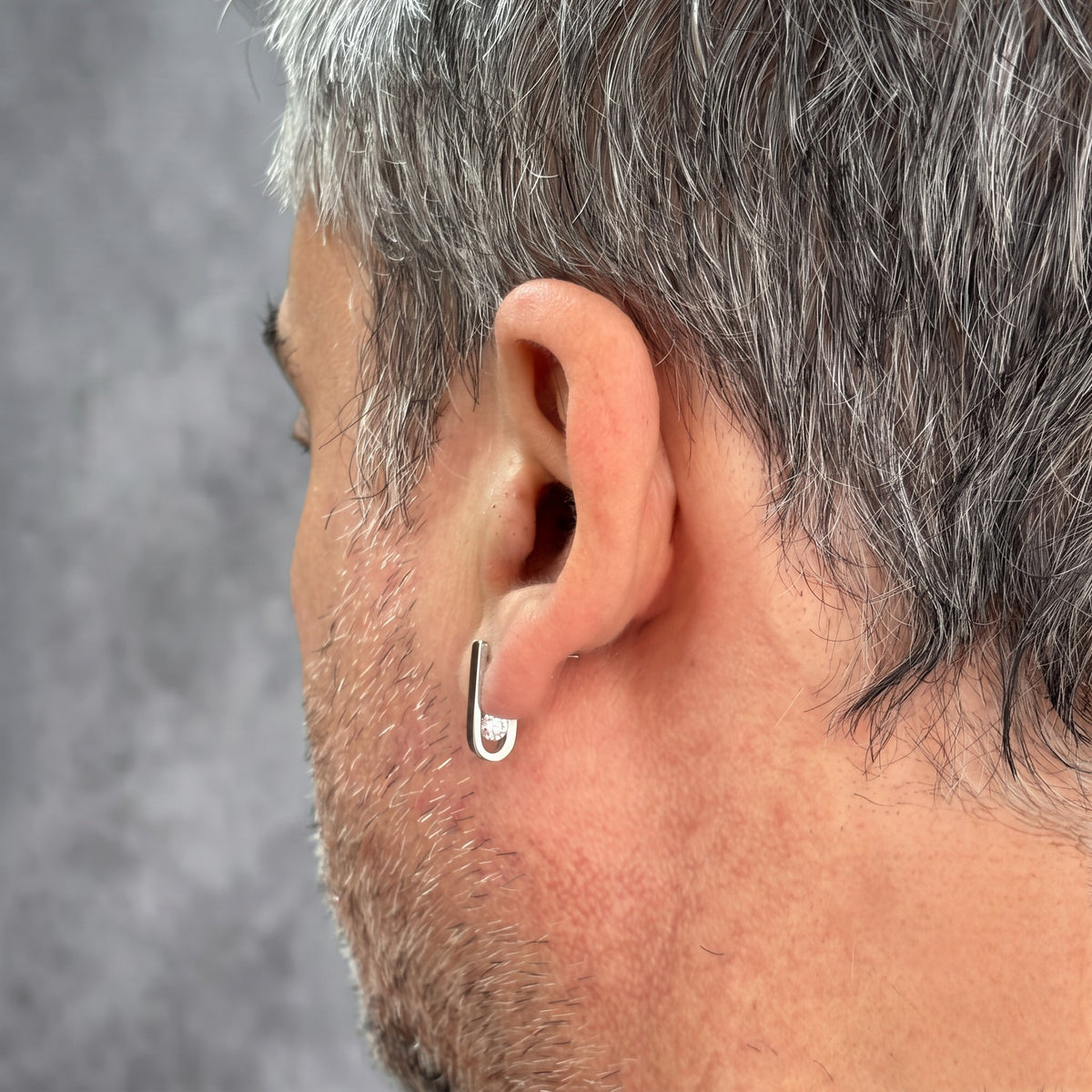 Back view of the J-02 earring on a male model's ear: the curve and clear zircon behind the earlobe