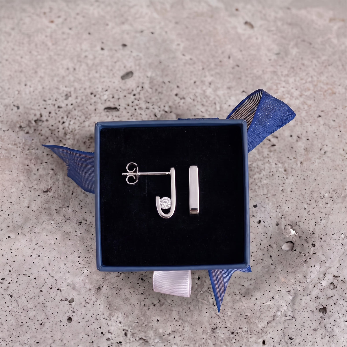 Pair of J-02 silver earrings in a navy gift box with a blue ribbon, on concrete