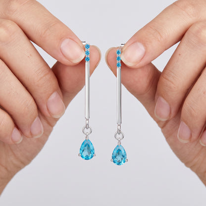Blue zircon drop earrings held between fingers – rhodium plated 925 silver post earrings