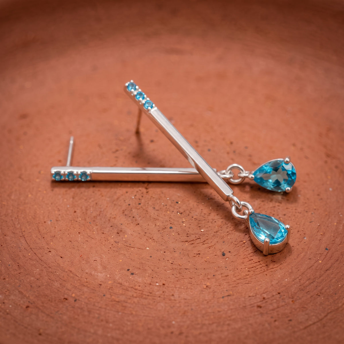 Blue drop earrings on a terracotta dish – earring post and prong-set teardrop zircon detail