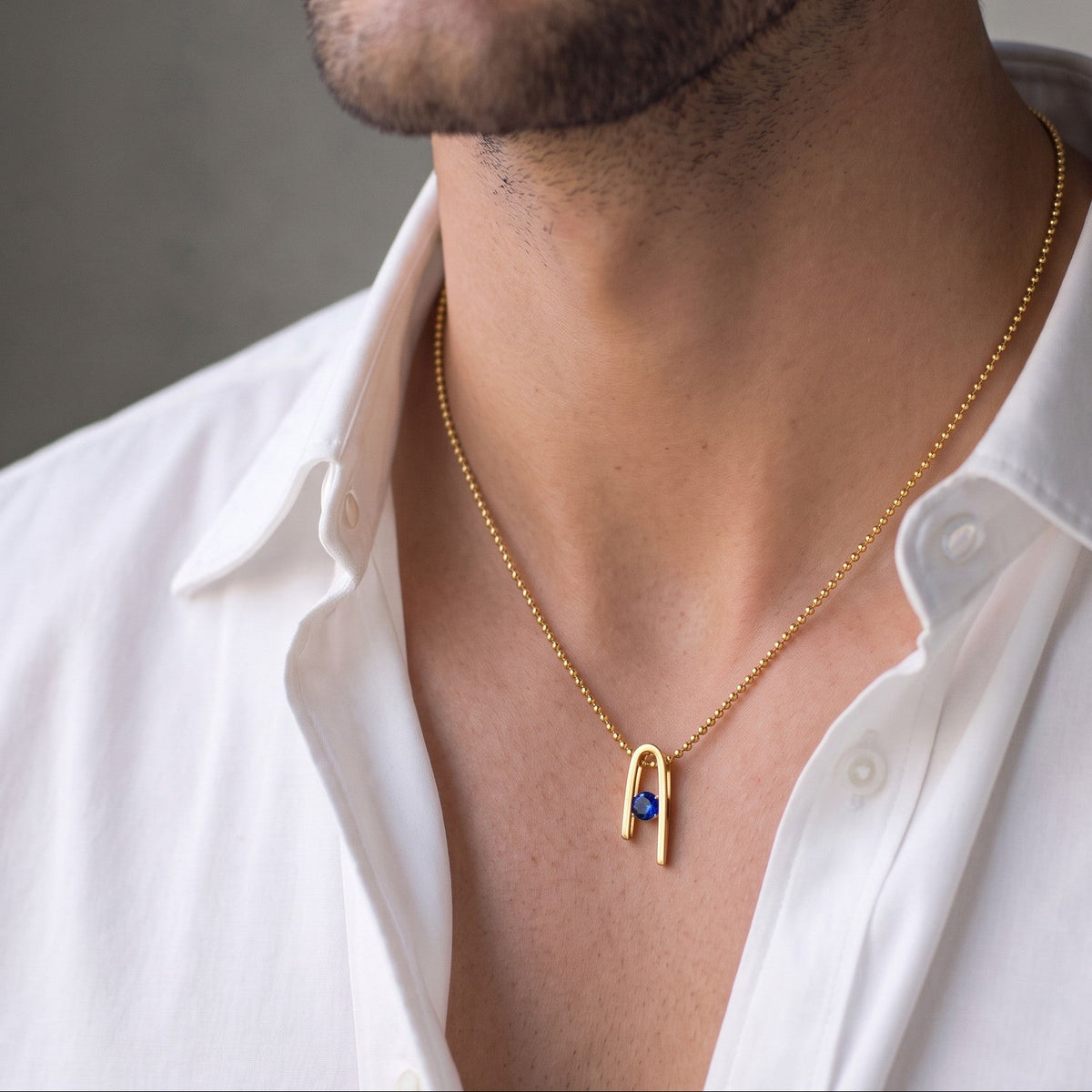 14K gold plated Minimalist n Necklace with its deep blue zircon, worn by a male model in a white shirt