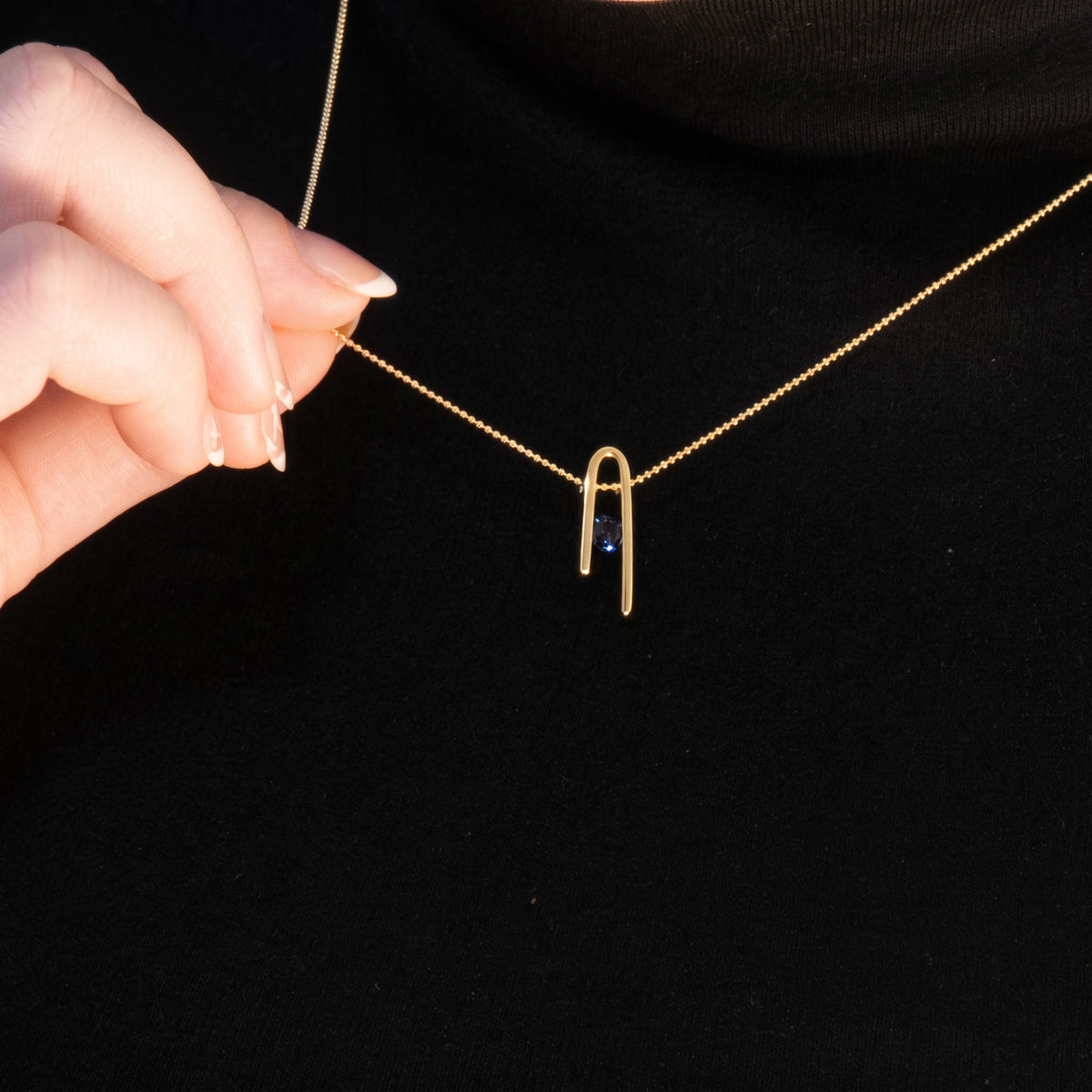 14K gold plated Minimalist n Necklace worn over a black sweater; a hand holds the chain