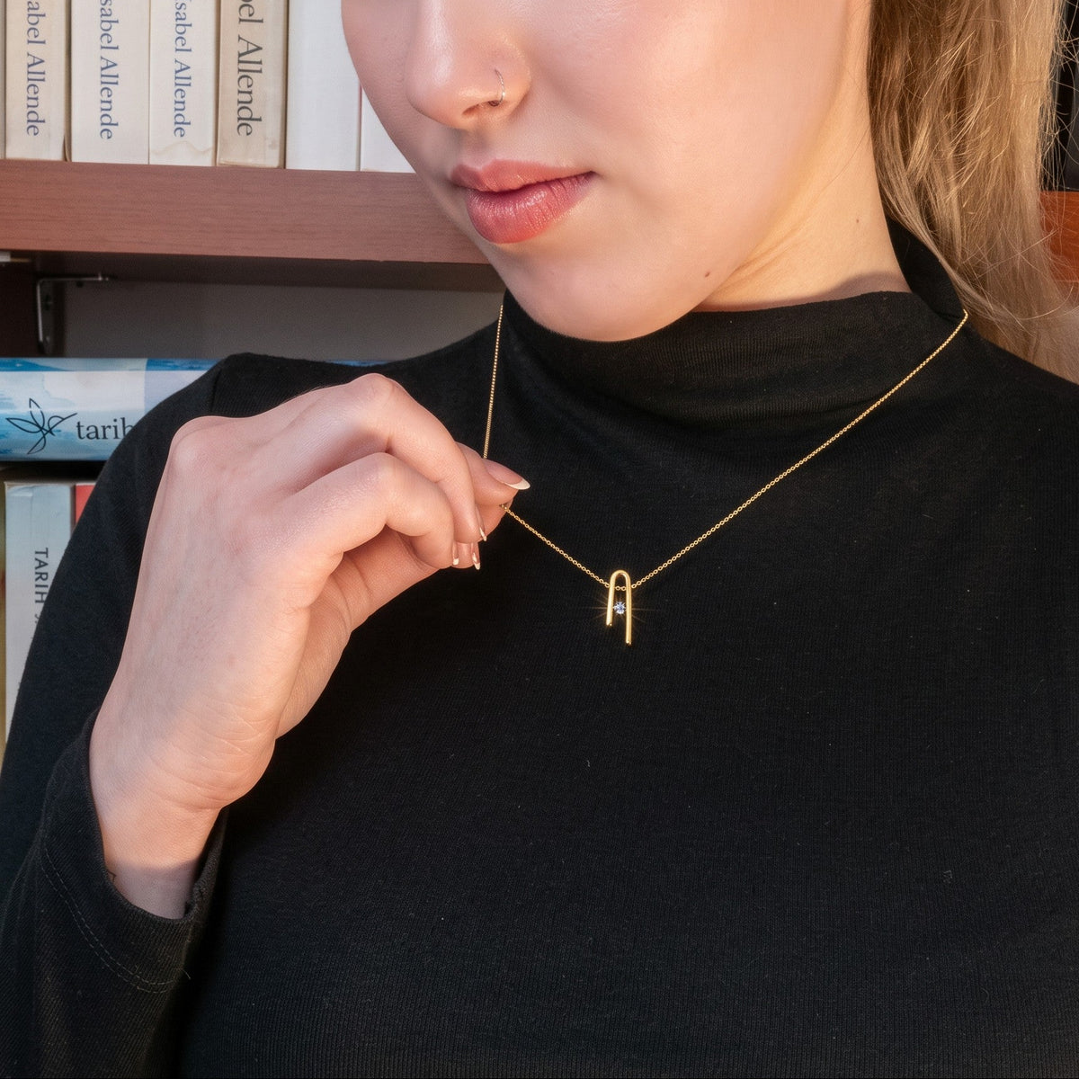 14K gold plated Minimalist n Necklace worn by a woman in a black turtleneck, in front of a bookshelf