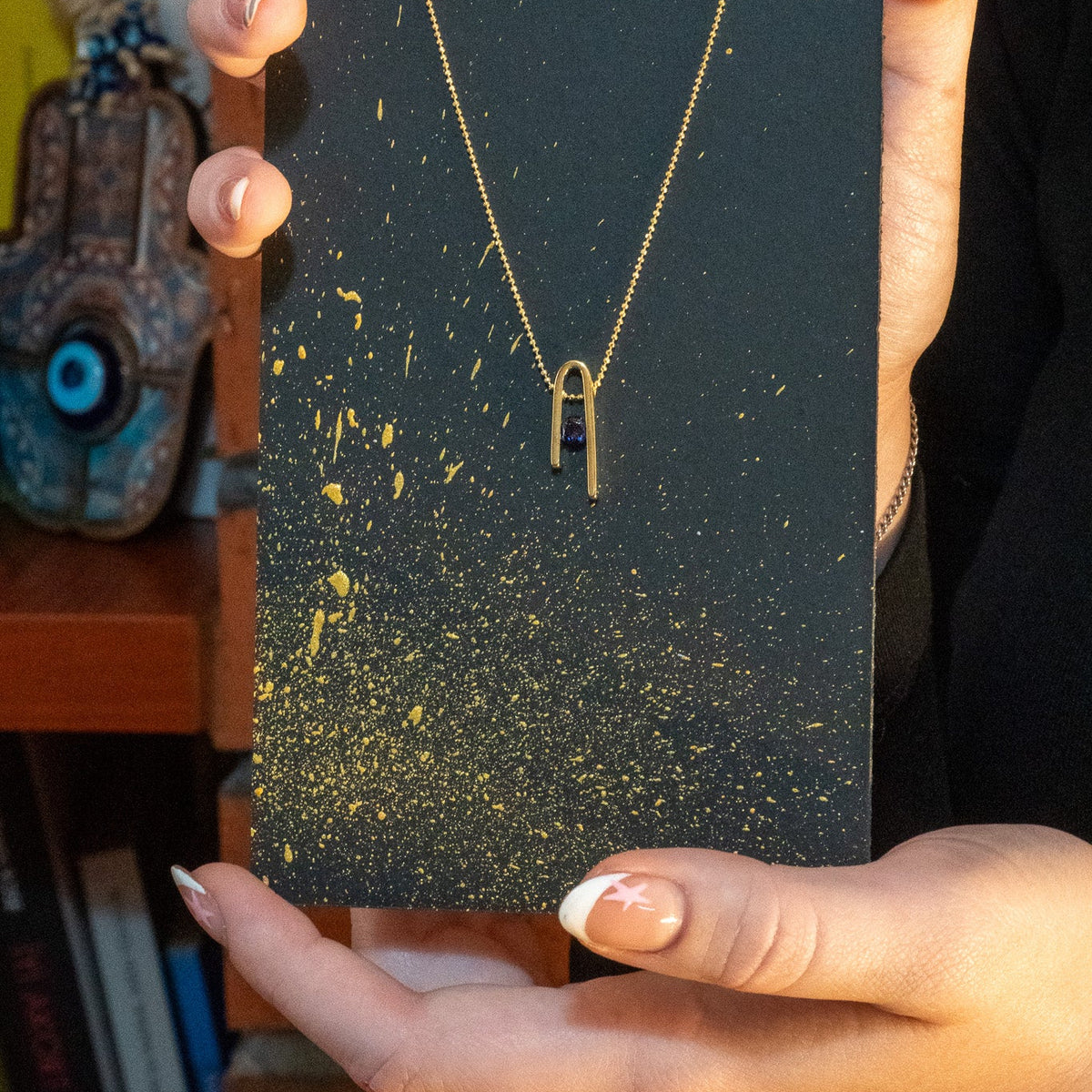 Minimalist n Necklace hanging in front of a black card speckled with gold