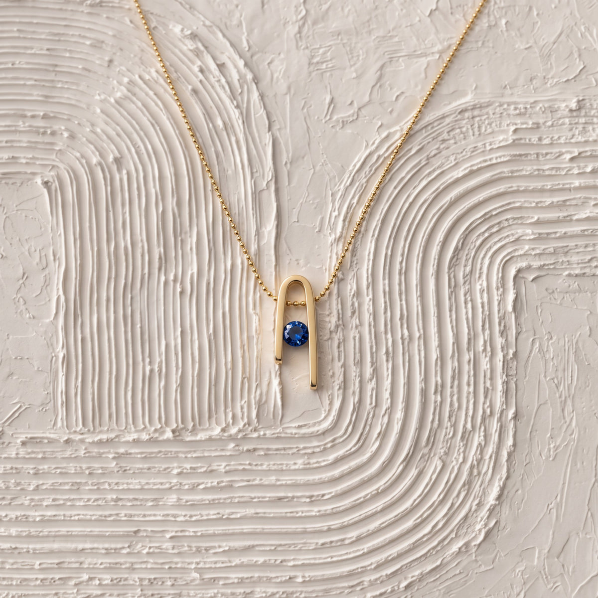 14K gold plated Minimalist n Necklace and its deep blue zircon on a white textured surface