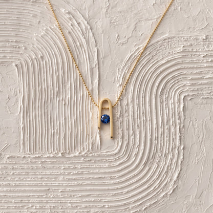 14K gold plated Minimalist n Necklace and its deep blue zircon on a white textured surface