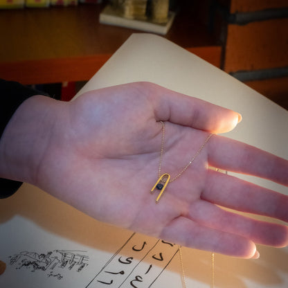 14K gold plated Minimalist n Necklace pendant with its deep blue zircon, resting in the palm of a hand
