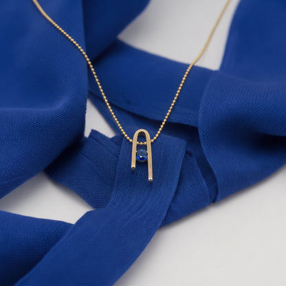 14K gold plated Minimalist n Necklace with its deep blue zircon on blue fabric