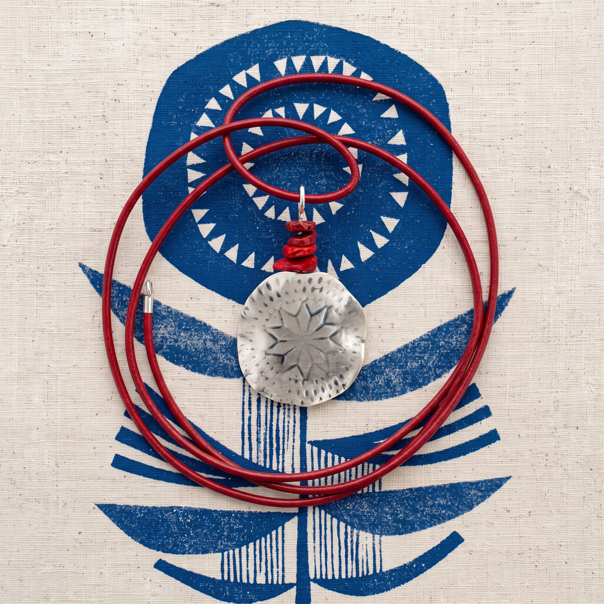 Polaris Necklace flat lay on navy printed fabric - shown with its red rubber cord